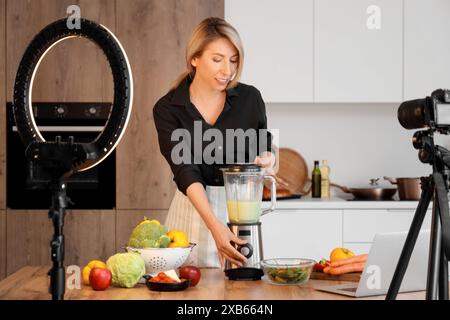 Food blogger donna che produce frullati di verdure mentre registra video in cucina Foto Stock