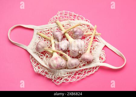 Borsa a cordoncino con teste d'aglio su sfondo rosa brillante, vista dall'alto Foto Stock