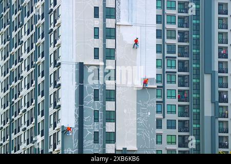 Tre dei lavoratori che eseguono l'accesso alla corda dipingono la facciata di un alto edificio residenziale Foto Stock