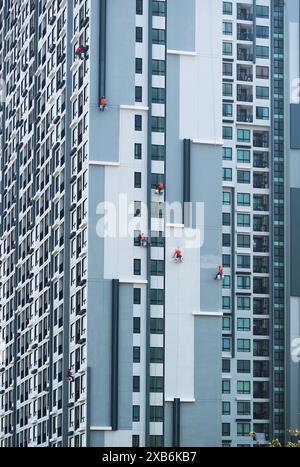 Gruppo di lavoratori industriali che si arrampicano dipingendo la facciata di un alto edificio moderno Foto Stock