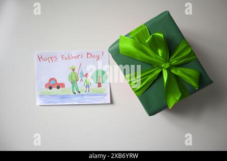 Festa del papà foto di una cartolina disegnata da un bambino. Un regalo di colore verde con un fiocco. Sfondo bianco. La cartolina mostra un padre e un figlio a pescare. AF Foto Stock