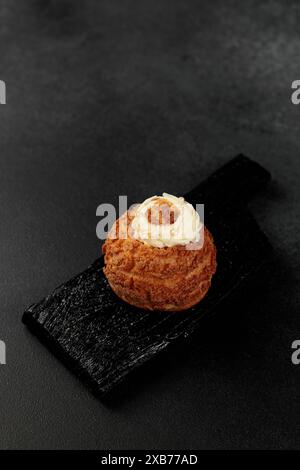 Torta Shu classica (choux). Impasto crema pasticcera a base di burro e latte, ripieno classico con crema aggiunta su un tagliere nero Foto Stock