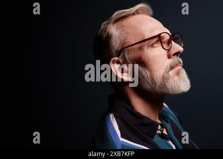 Ritratto con vista laterale di un anziano barbuto che indossa gli occhiali su sfondo scuro, spazio copia Foto Stock