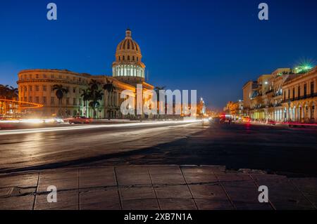 Raffigura una vivace strada della città di notte che conduce ad un grande edificio illuminato a cupola. L'esposizione lunga cattura le tracce di luce del movimento Foto Stock