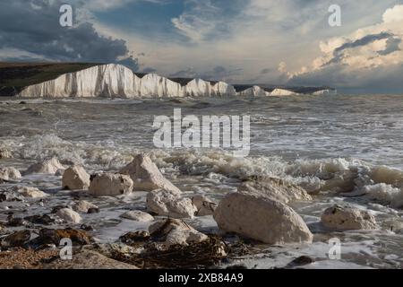 Le onde del tramonto si infrangono contro le bianche scogliere sotto un cielo blu con nuvole Foto Stock