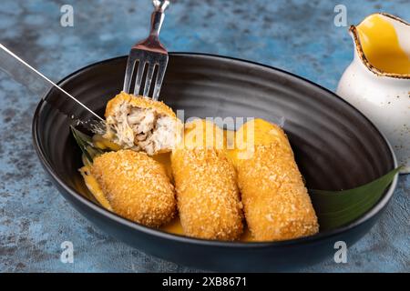 Pelo di snack di pollo impanato sul piatto nero sullo sfondo blu. Sezione trasversale di un bastoncino di patatine fritte Foto Stock