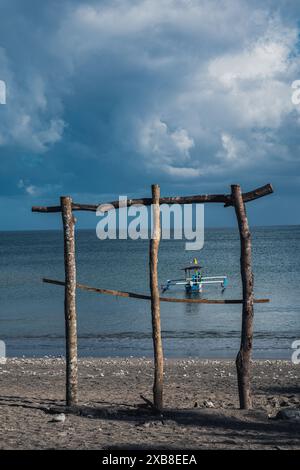 Una piccola barca è ormeggiata sulla spiaggia sabbiosa dietro rami di legno Foto Stock