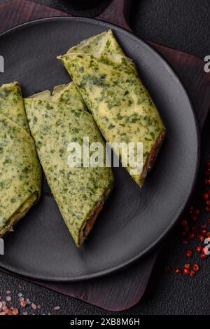 Deliziosi pancake fatti in casa con spinaci, salmone, formaggio Philadelphia con sale, spezie ed erbe aromatiche su sfondo di cemento scuro Foto Stock