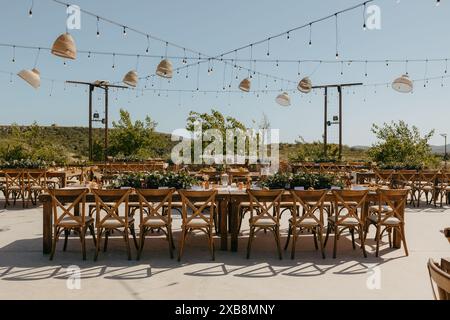 Un tavolo da pranzo all'aperto decorato con una varietà di grandi lampadine e sedie sospese Foto Stock