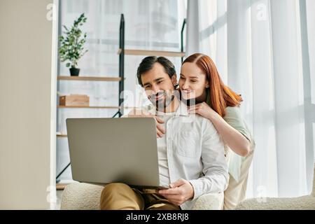 Una donna rossa e un uomo barbuto si rilassano su un divano, circondati dallo schermo di un notebook. Foto Stock