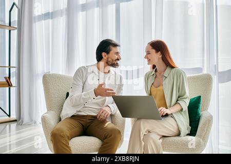 Una coppia elegante, una donna rossa e un uomo barbuto, seduto su una sedia, coinvolto in una conversazione su un notebook. Foto Stock