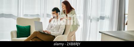 Una donna rossa e un uomo barbuto seduti su un divano, coinvolti nell'utilizzo di un laptop nel loro elegante appartamento. Foto Stock