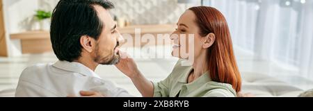 Una donna rossa e un uomo barbuto condividono un momento tenero mentre si guardano negli occhi degli altri in un appartamento moderno. Foto Stock