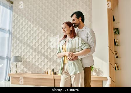 La donna rossa e l'uomo barbuto stanno insieme in un salotto moderno, trascorrendo del tempo di qualità in un ambiente accogliente. Foto Stock