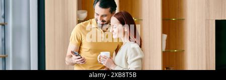 Un uomo barbuto e una donna rossa invischiati nel loro telefono, che condividono un momento di connessione digitale nel loro moderno appartamento. Foto Stock
