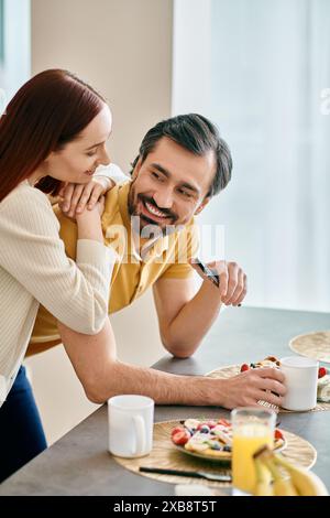 Una donna rossa e un uomo barbuto condividono la colazione mentre abbracciano il loro moderno appartamento, connettendosi intimamente. Foto Stock