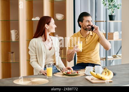 Donna rossa e uomo barbuto che chiacchierano al telefono mentre facevano colazione in un appartamento moderno. Foto Stock