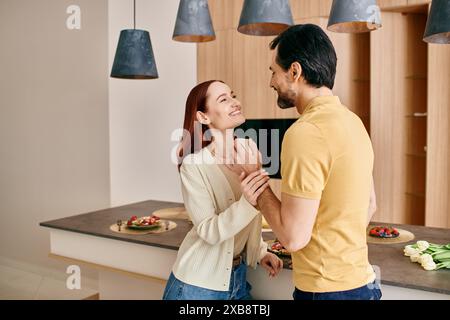 Una donna rossa e un uomo barbuto stanno in una cucina moderna, condividendo un momento di connessione e vicinanza. Foto Stock