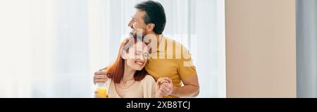 La donna rossa e l'uomo barbuto condividono un abbraccio di cuore, crogiolandosi nel calore del loro amore in un appartamento moderno. Foto Stock