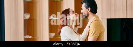 Una donna rossa e un uomo barbuto condividono un caldo abbraccio nella loro moderna cucina, godendosi un momento di amore e di amicizia. Foto Stock