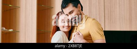 Una bella coppia adulta, una donna rossa e un uomo barbuto condividono un profondo abbraccio nel loro salotto moderno. Foto Stock