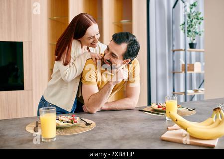 Una bella donna rossa e un uomo barbuto che si godono una tranquilla colazione insieme nella loro cucina moderna. Foto Stock