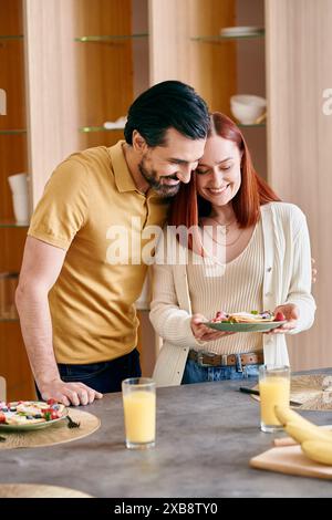 Una donna rossa e un uomo barbuto stanno insieme in una cucina moderna, godendosi momenti di qualità a casa. Foto Stock
