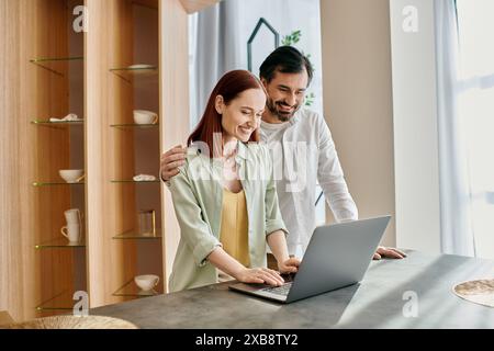 Una coppia, la donna con i capelli rossi e l'uomo con la barba, avvolto in un portatile, che si legano nel loro moderno appartamento. Foto Stock