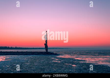 Un tramonto tranquillo dipinge il cielo sopra una torre solitaria vicino all'acqua. Foto Stock