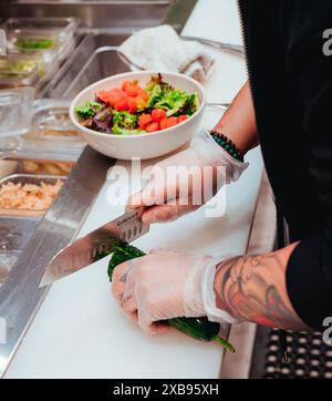 Una persona che prepara l'insalata, mentre taglia il cetriolo in un'area ristoro affollata Foto Stock