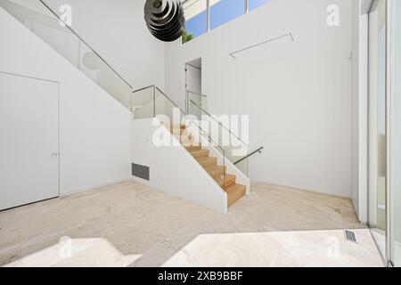 L'interno di una casa bianca contemporanea con ringhiere in vetro curvo e scala in legno Foto Stock