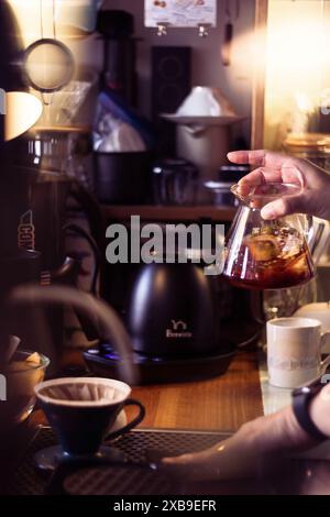 Un barista che prepara un caffè da versare in un bar accogliente e ben attrezzato Foto Stock