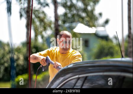 Getto d'acqua ad alta pressione per auto lavaggio uomo con messa a fuoco selettiva all'autolavaggio. Foto Stock