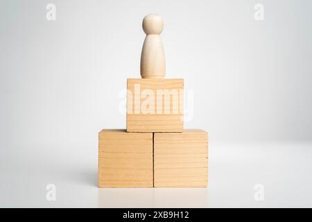 Una figura di legno si erge sopra tre blocchi di legno. I blocchi sono impilati uno sopra l'altro, con il blocco più alto in basso e il pantaloncino Foto Stock
