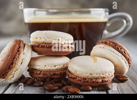 Macaron aromatizzati al caffè impilati su fondo in legno con tazza da caffè e fagioli. Foto Stock