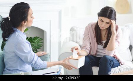 Consulente che offre tessuti durante la sessione di terapia emotiva in Bright Room Foto Stock