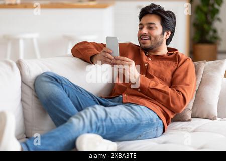 Giovane uomo che si rilassa sul divano utilizzando lo smartphone Foto Stock