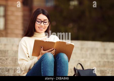 Donna seduta sui gradini che legge un libro, che fa i compiti Foto Stock
