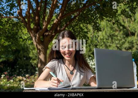 Giovane ragazza del college sorridente e interagisce con il suo portatile a un tavolo del campus. Inizio del college, tecnologia, vita studentesca, istruzione Foto Stock