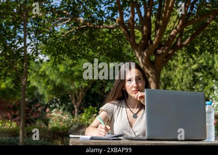 Giovane ragazza universitaria con un'espressione premurosa in una riunione virtuale, seduta a un tavolo nel campus. Studente concentrato, notebook, inizio dell'universit Foto Stock