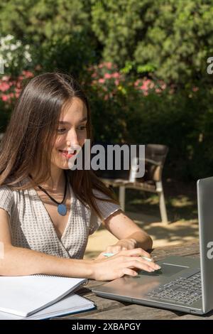 Ragazza del college seduta a un tavolo del campus sorridente e che usa il suo laptop. Vita accademica, tecnologia, istruzione, ambiente universitario Foto Stock