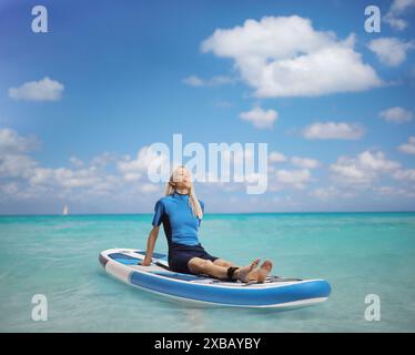 Donna in muta che prende il sole su una tavola di sup in mare Foto Stock