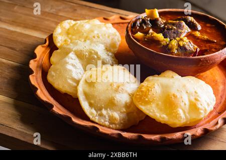 luchi o puri e curry di montone o laal maas serviti su piatto di terra. Il luchi è una focaccia indiana fatta di farina e fritta in profondità. tradizionale pasto indiano. Foto Stock