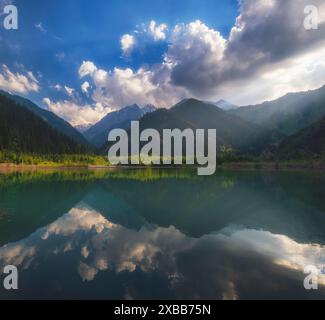 un bellissimo lago di montagna con acque turchesi cristalline che riflette il paesaggio circostante, le montagne, la foresta e le nuvole galleggianti Foto Stock