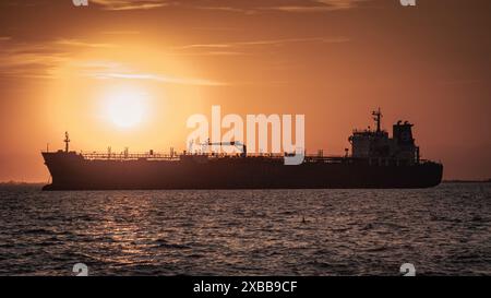 Maestosa nave sagomata contro un tramonto infuocato. Questa immagine cattura l'impressionante vista di una grande nave da carico che rimane al porto. Foto Stock