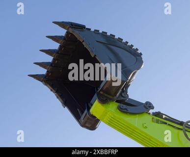 Paletta e braccio idraulico di un escavatore, isolato su sfondo blu chiaro, ripresa prospettica ad angolo basso. Foto Stock