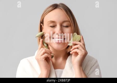 Donna con rullo per massaggi e guasha su sfondo grigio Foto Stock