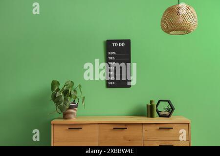 Decorazioni su cassettiera in legno e asse con una lista delle cose da fare su una parete verde in un elegante interno del soggiorno Foto Stock