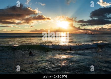 Il sole tramonta sull'oceano, proiettando un caldo bagliore sull'acqua. Una piccola barca è visibile in lontananza nel tranquillo paesaggio. Il cielo ha un soffice c Foto Stock