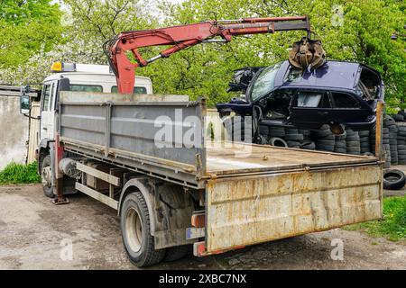 Una pala idraulica carica un relitto abbandonato su un camion per portarlo in un sito di riciclaggio, smaltimento di auto usate, processo di caricamento dei relitti Foto Stock